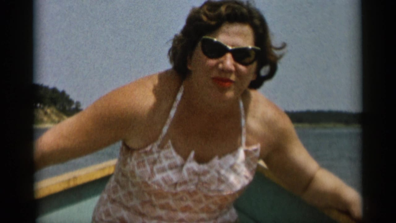 The woman stands or leans in the boat, wearing dark sunglasses and a pink-and-white swimsuit with Cape Cod water in the background.