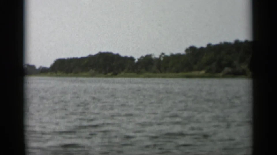 1956 Cape Cod home-movie frame showing calm water and a tree-lined shore viewed from a moving boat.