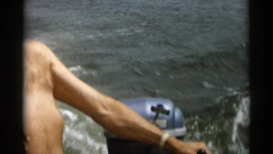 1956 Cape Cod home-movie frame showing an adult man steering a small motorboat with an outboard motor churning the water.