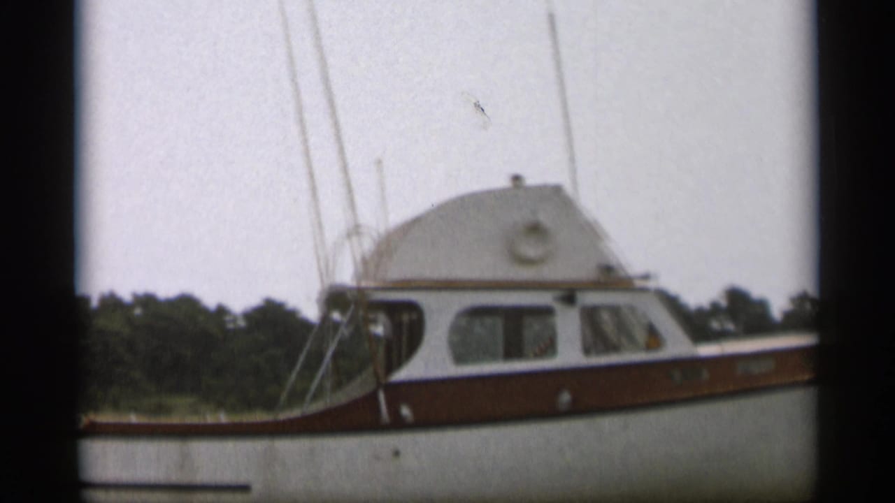 A 1956 Cape Cod home-movie frame shows a white and brown cabin motorboat at close range on calm water.