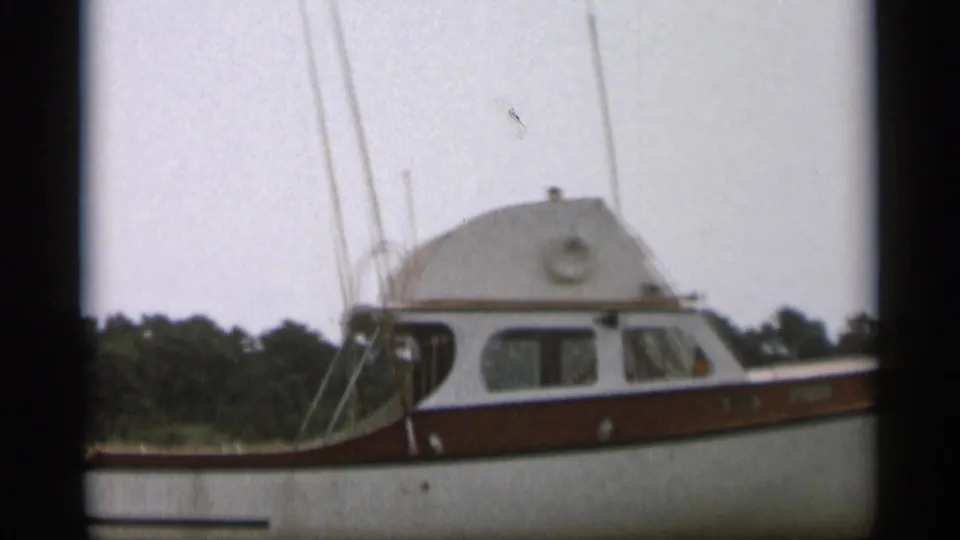 A 1956 Cape Cod home-movie frame shows a white and brown cabin motorboat at close range on calm water.