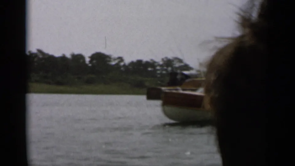 A Cape Cod motorboat moves away from the camera, partially obscured by a dark foreground shape, leaving disturbed water behind.