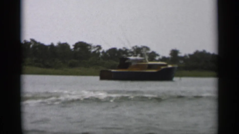 The motorboat appears farther out on Cape Cod water, with a soft wake in the foreground and trees along the far shore.