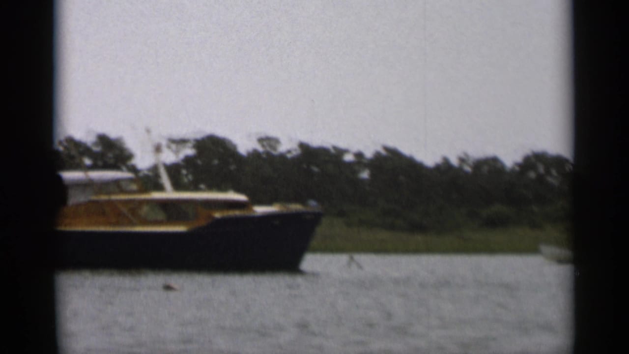 Cabin boat closer to frame center on water with trees in the background.