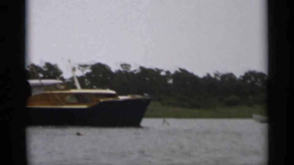 The Cape Cod home-movie frame shows a cabin cruiser passing across the water against a dark green shoreline.