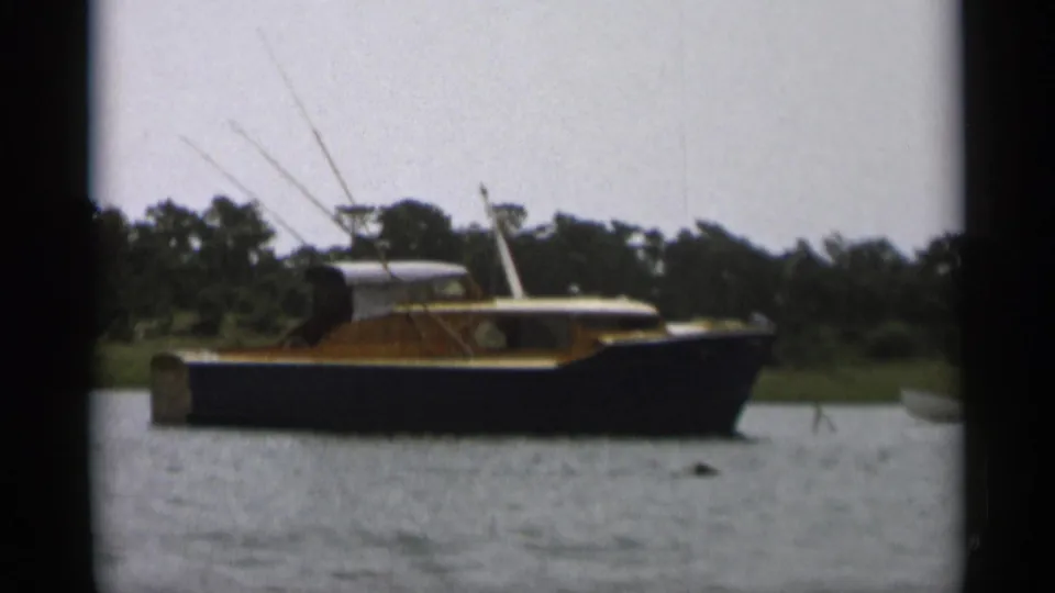 A dark-hulled cabin boat fills more of the 8mm frame, with Cape Cod shoreline trees and rippled water visible.
