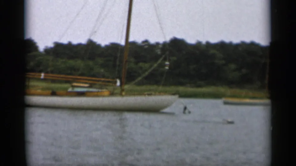 The final 1956 Cape Cod frame shows a sailboat moored or moving slowly near a wooded shore on calm water.