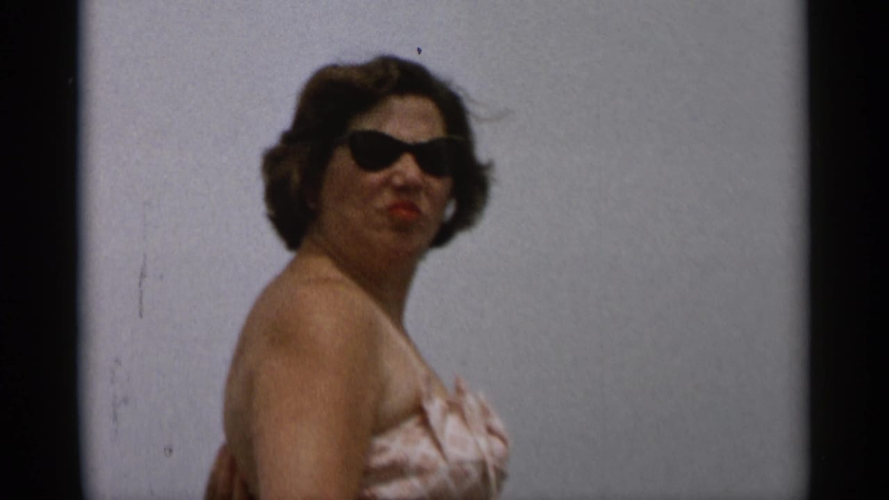 The woman turns slightly in a strapless swimsuit and dark sunglasses, with mid-century styling visible in the Cape Cod footage.