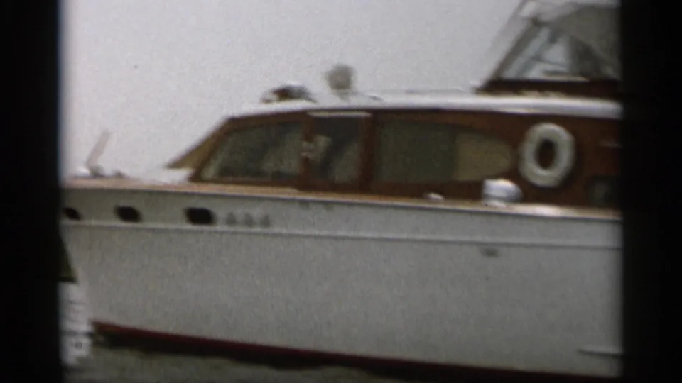 A white motorboat with wood trim sits on calm water, continuing the Cape Cod 1956 summer boating sequence.