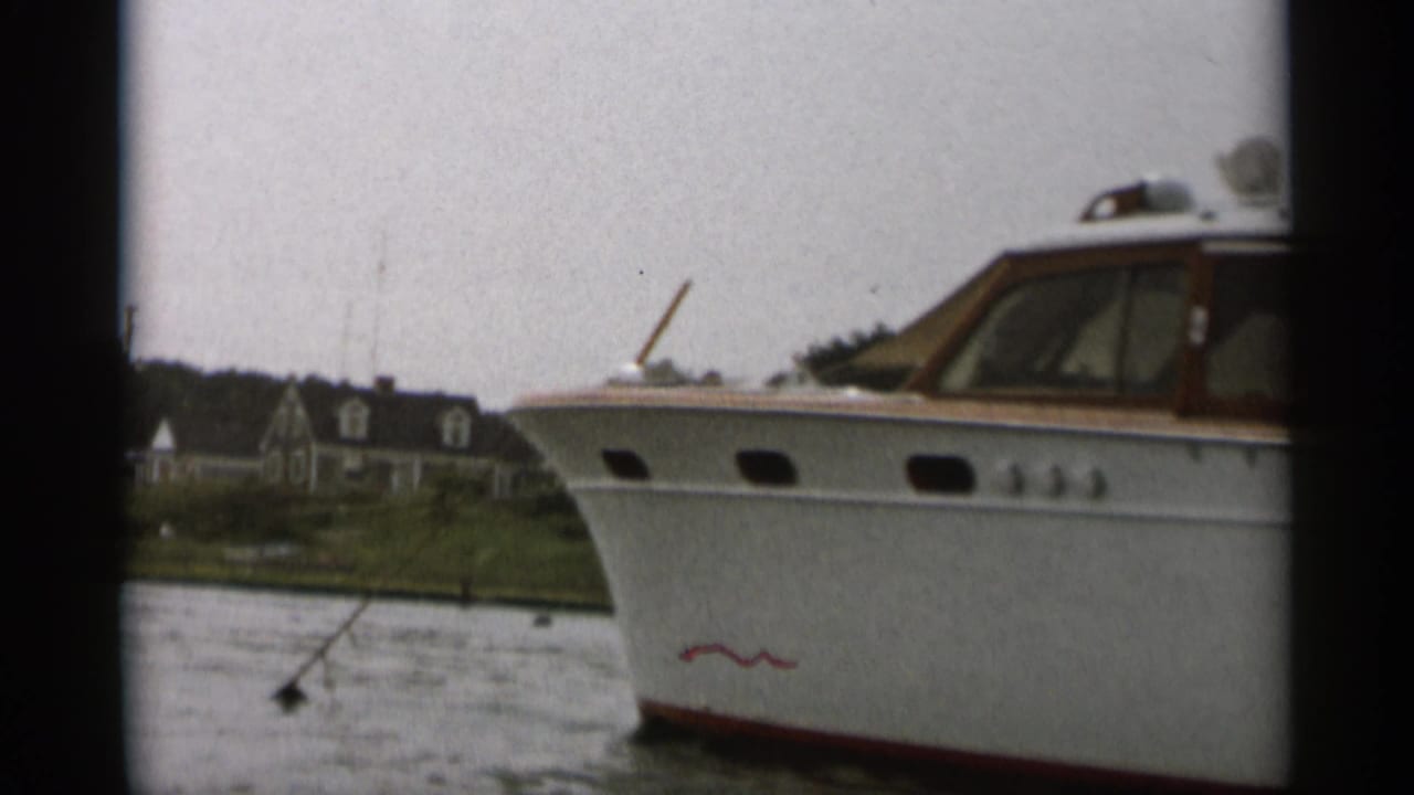 White motorboat with wood-trimmed cabin cruising near a low shoreline.