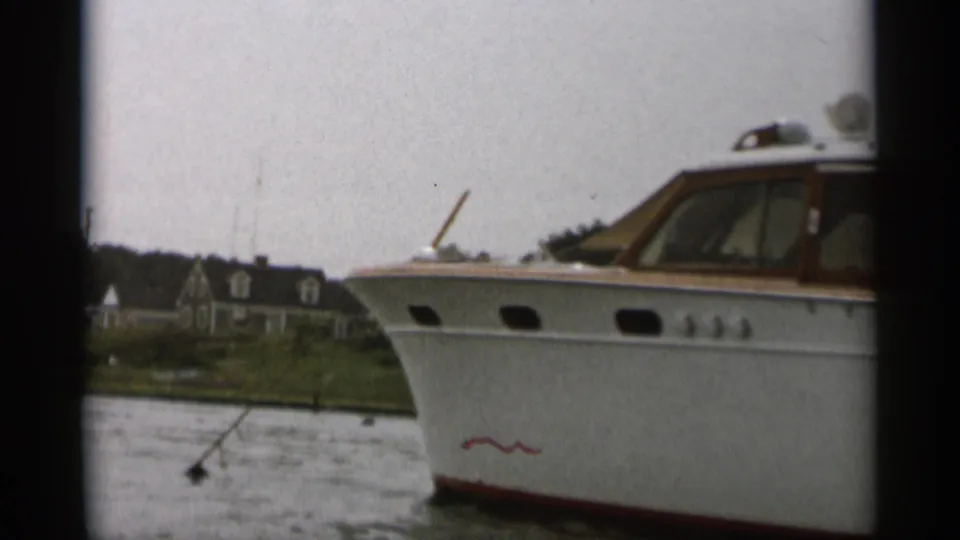 1956 Cape Cod home-movie frame showing a white cabin motorboat with wood trim moving past a distant shoreline.