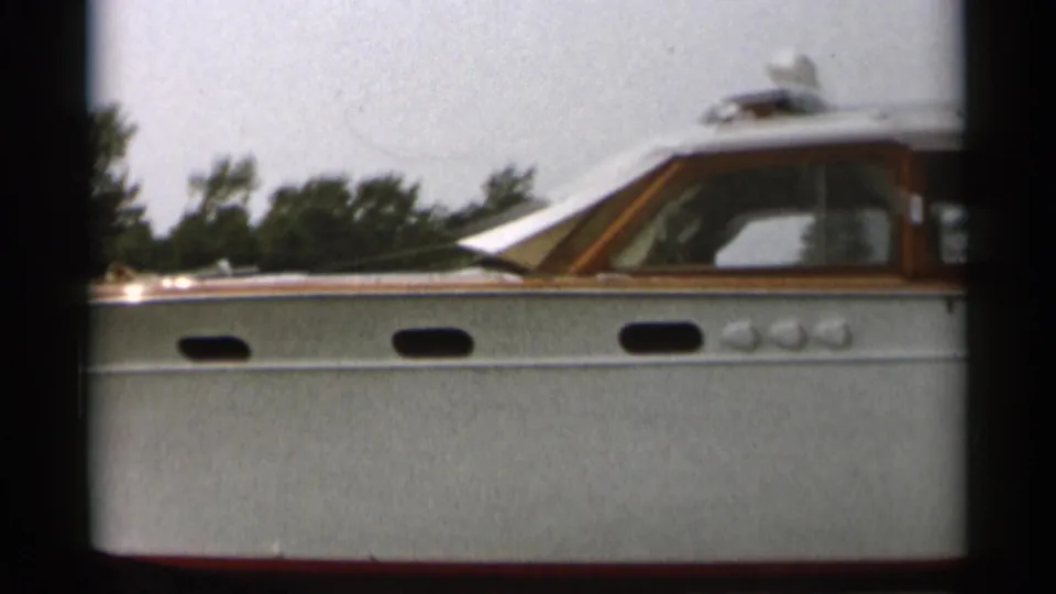 Close side view of the 1950s Cape Cod motorboat, showing oval portholes, white hull, and varnished cabin trim.