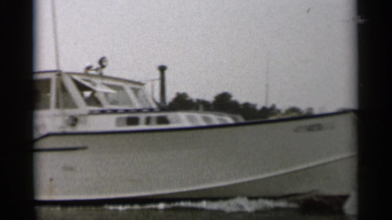 White cabin motorboat moving across water with shoreline trees behind it.