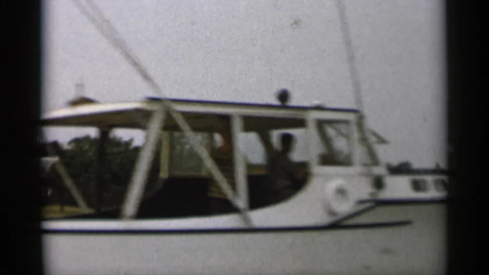 1956 Cape Cod home-movie view of the white motorboat cabin, showing a seated passenger and the boat structure in soft 8mm detail.