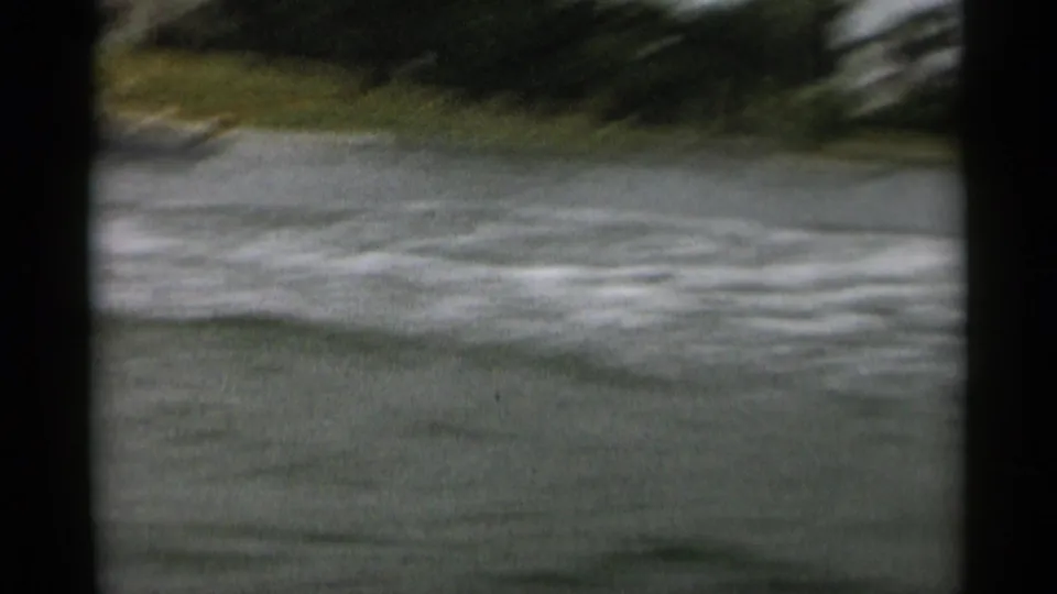 Soft 8mm frame from the Cape Cod boat sequence showing water, wake, and a low shoreline after the motorboat moves out of view.