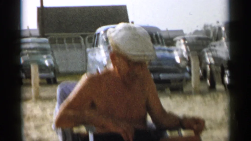 The final frame is softly blurred as the older man remains seated on the Cape Cod beach near parked 1950s cars.