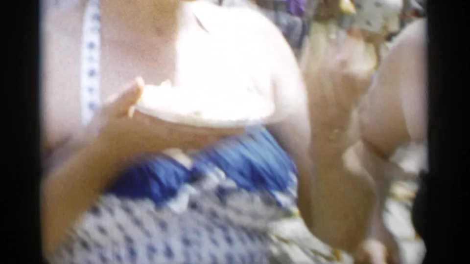 At Jones Beach in 1956, a woman in a blue-and-white polka dot swimsuit holds food while other beachgoers stand nearby.