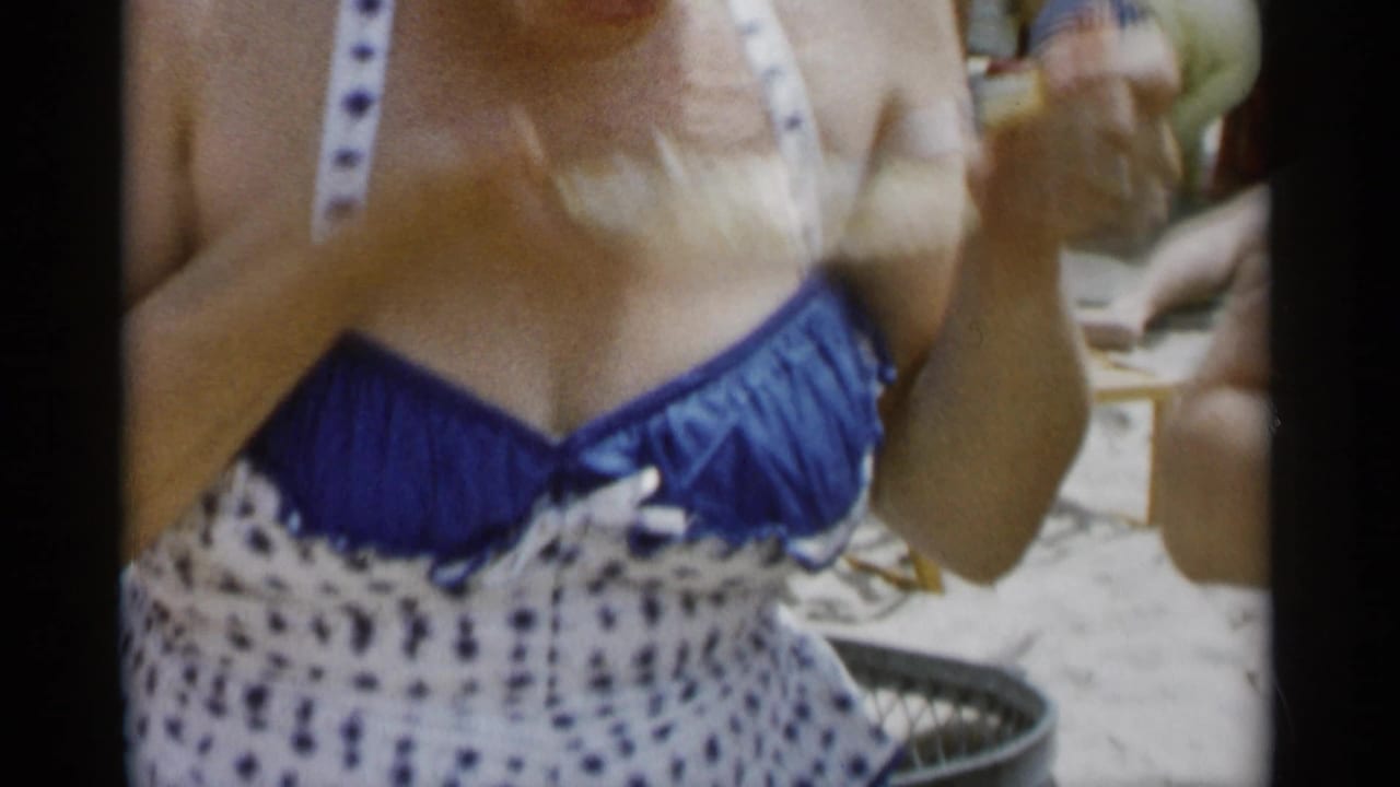 Close 1956 Jones Beach view of a woman in a blue-and-white polka dot swimsuit raising food during an eating contest.