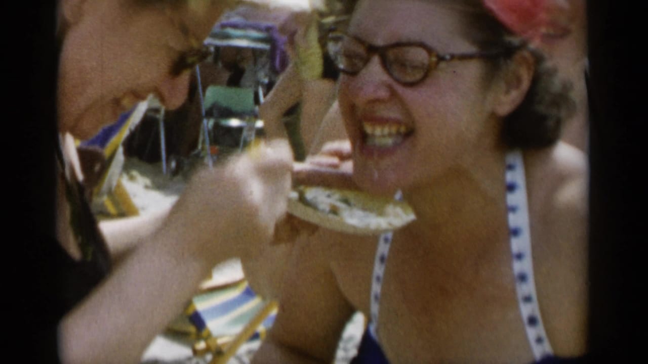 A smiling woman in glasses leans toward a bite of cake while seated among beach chairs at Jones Beach.