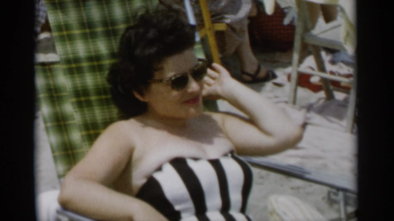 At Jones Beach in 1956, a woman in sunglasses and a black and white striped swimsuit reclines on a beach chair.