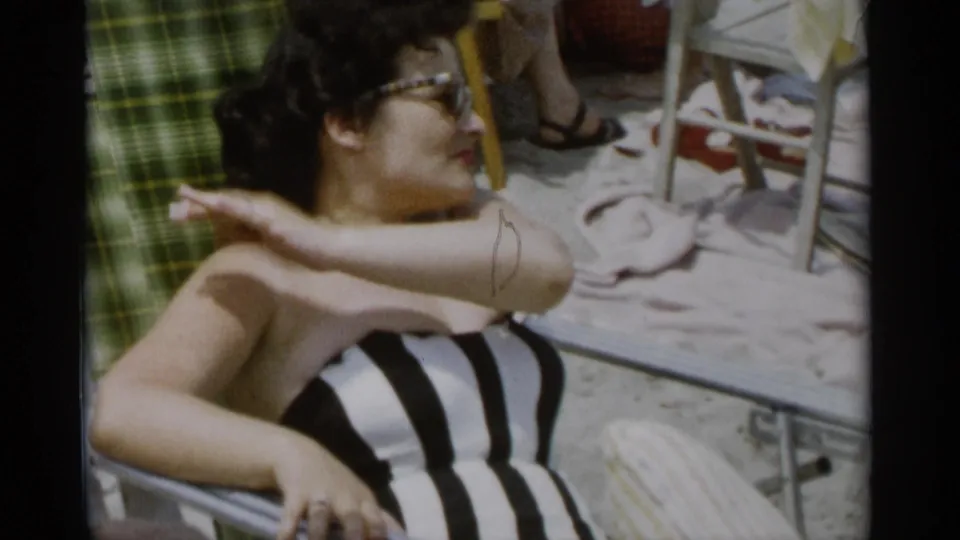 At Jones Beach in 1956, a woman in a striped swimsuit raises her arm while reclining on a lounge chair.