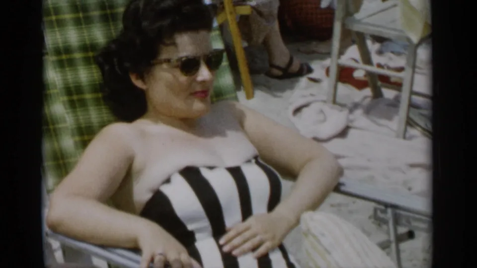 At Jones Beach in 1956, a woman in sunglasses rests on a lounge chair with beach towels and chairs around her.