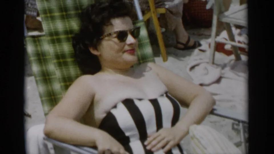 At Jones Beach in 1956, a woman in sunglasses and a black-and-white striped swimsuit relaxes on a green plaid beach chair.