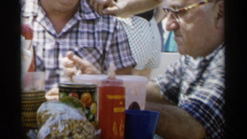 A 1956 Jones Beach picnic view shows the man in profile near a wrapped snack, food tin, red bottle, and blue cup.