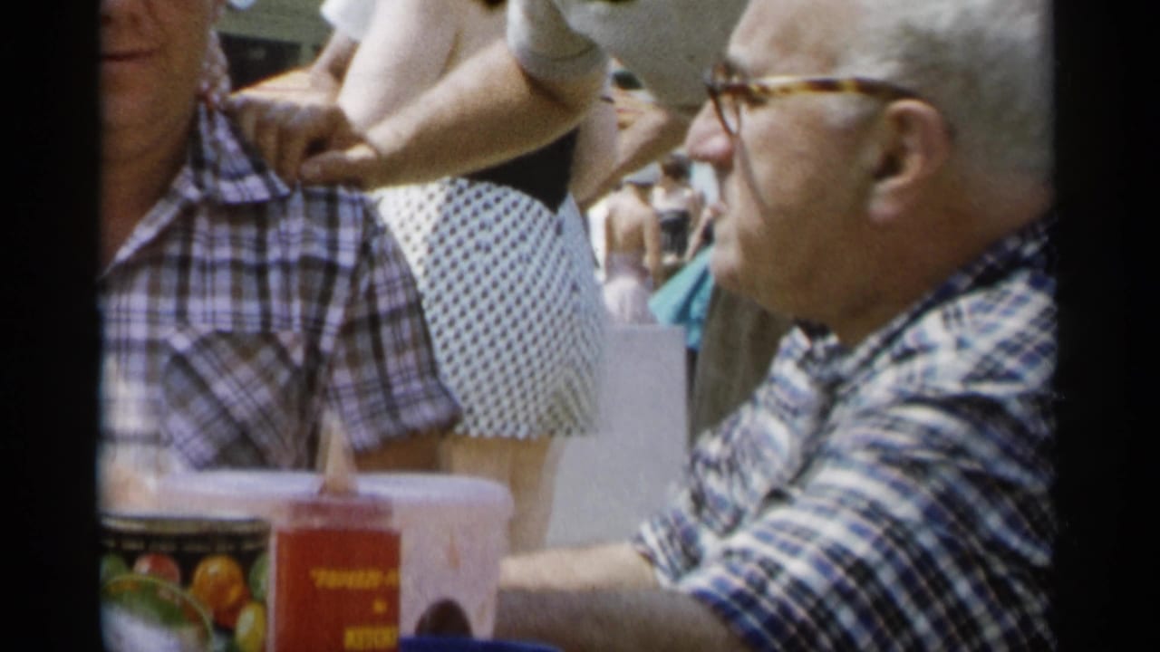 Two adult men sit at a picnic table with cups, a condiment bottle and a fruit can in front of them.