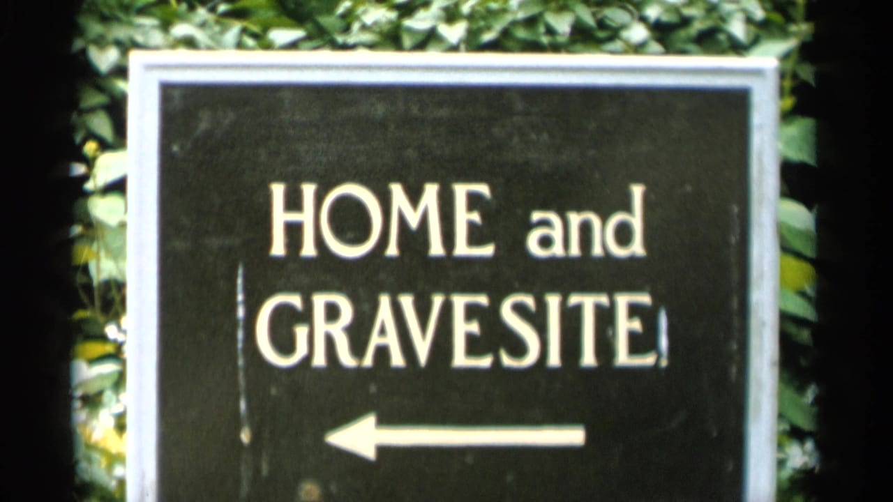 Black sign reading HOME and GRAVESITE with a left arrow against green foliage.