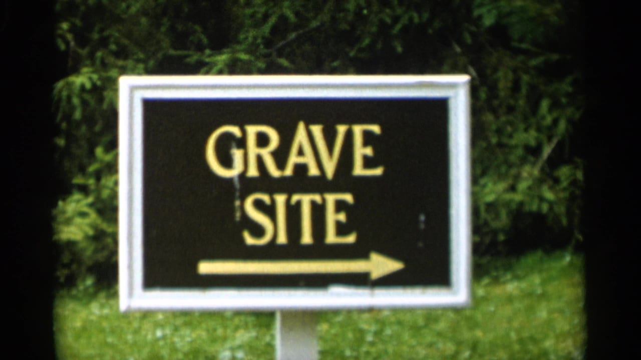 Black GRAVE SITE sign with a right arrow set in grass and trees.