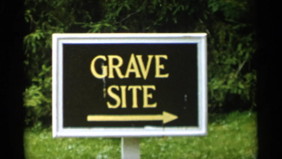 1956 Jones Beach frame showing a black GRAVE SITE sign with gold lettering and a right arrow beside trees and lawn.