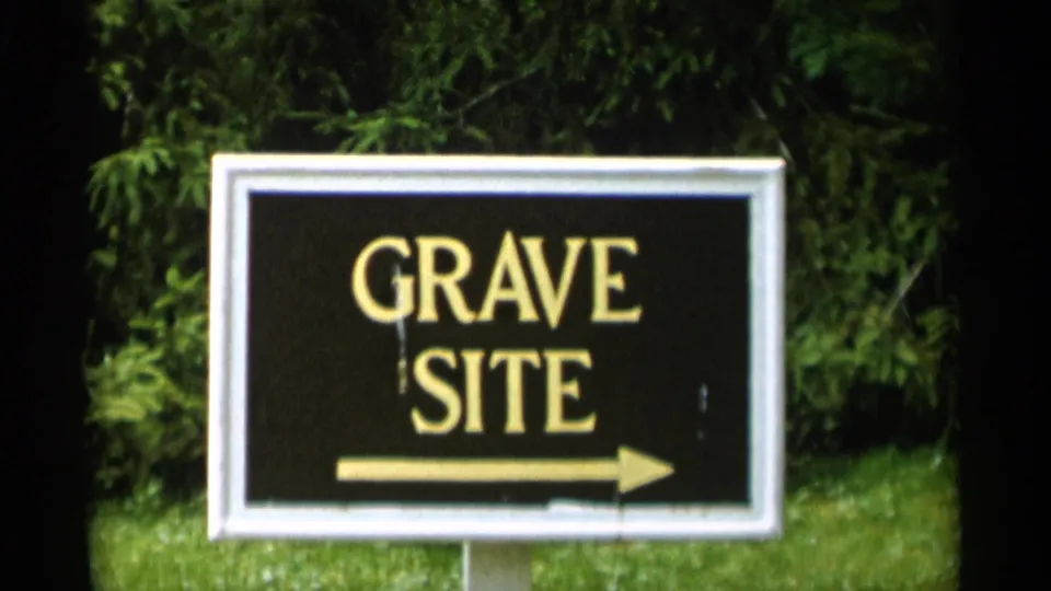 1956 Jones Beach home-movie frame with a closer GRAVE SITE directional sign and right arrow backed by shrubs and grass.