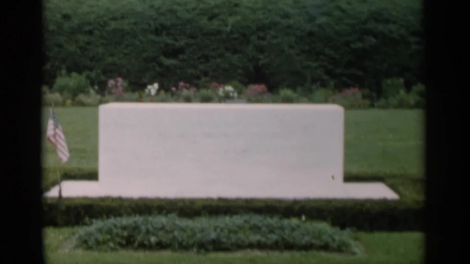 Jones Beach garden footage from 1956 showing a pale rectangular stone feature framed by lawn, hedges, flowerbeds, and a small flag.
