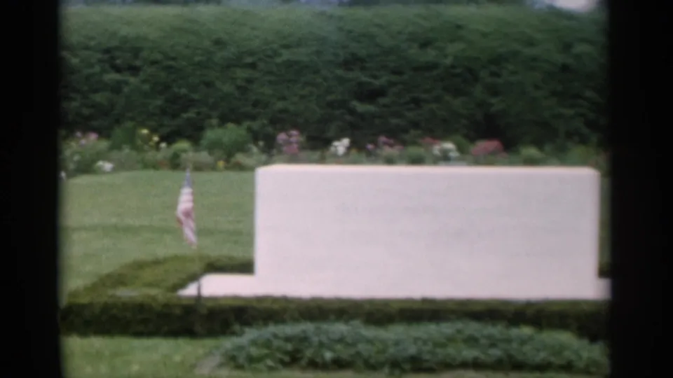 1956 Jones Beach frame centered on a white memorial-like marker with a small American flag in manicured grounds.