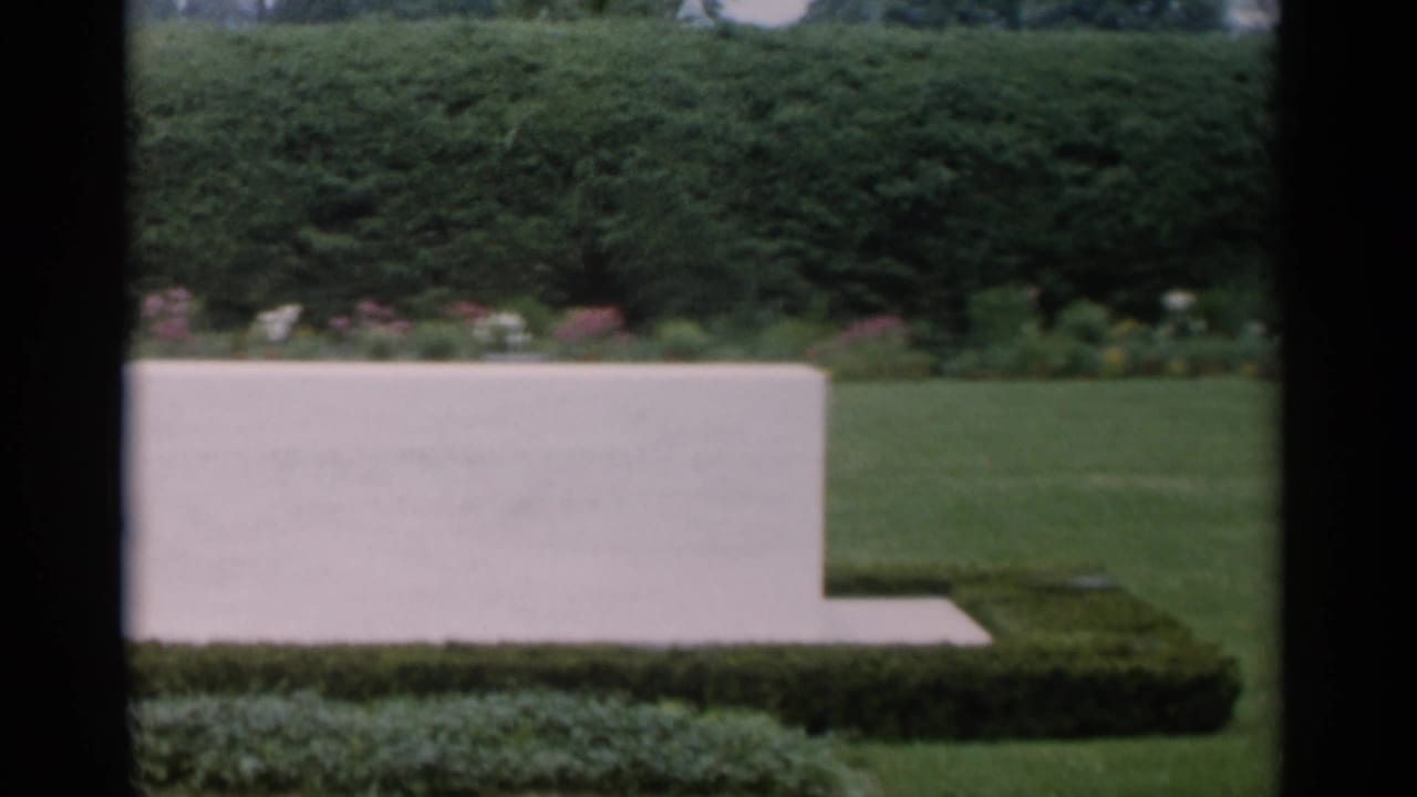 Low white stone marker in a Jones Beach garden, bordered by clipped hedges, lawn, and distant flower beds.