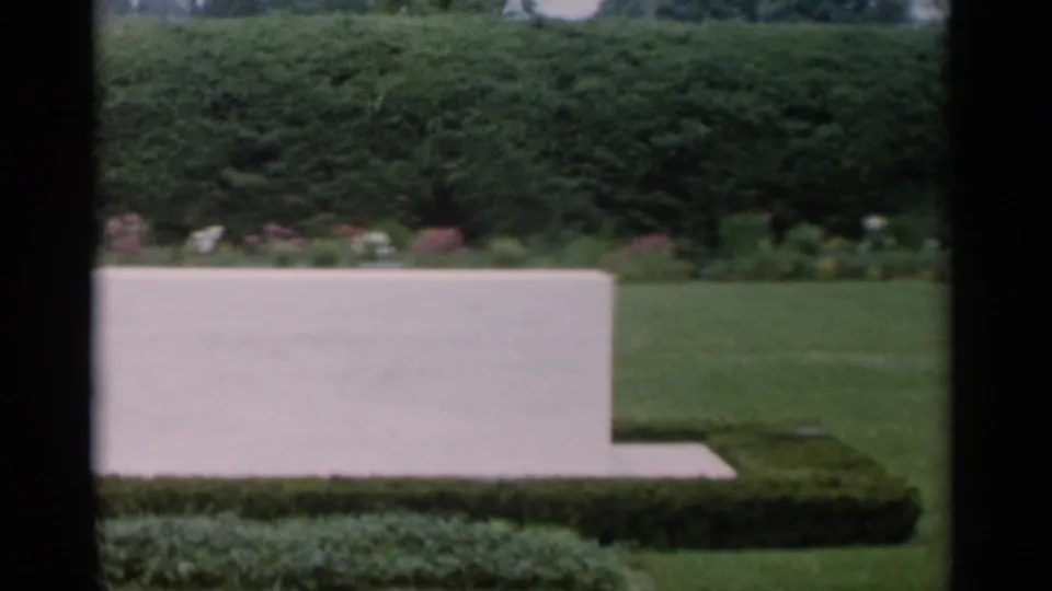 Low white stone marker in a Jones Beach garden, bordered by clipped hedges, lawn, and distant flower beds.