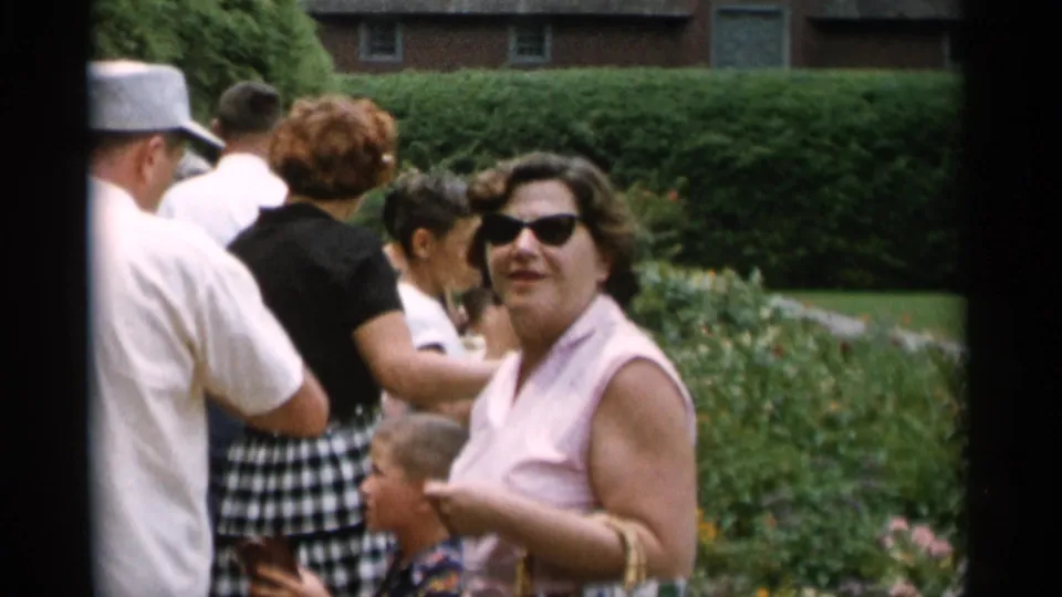 Jones Beach garden visitors in 1950s summer clothing, including a woman in sunglasses, stand near hedges and flower beds.