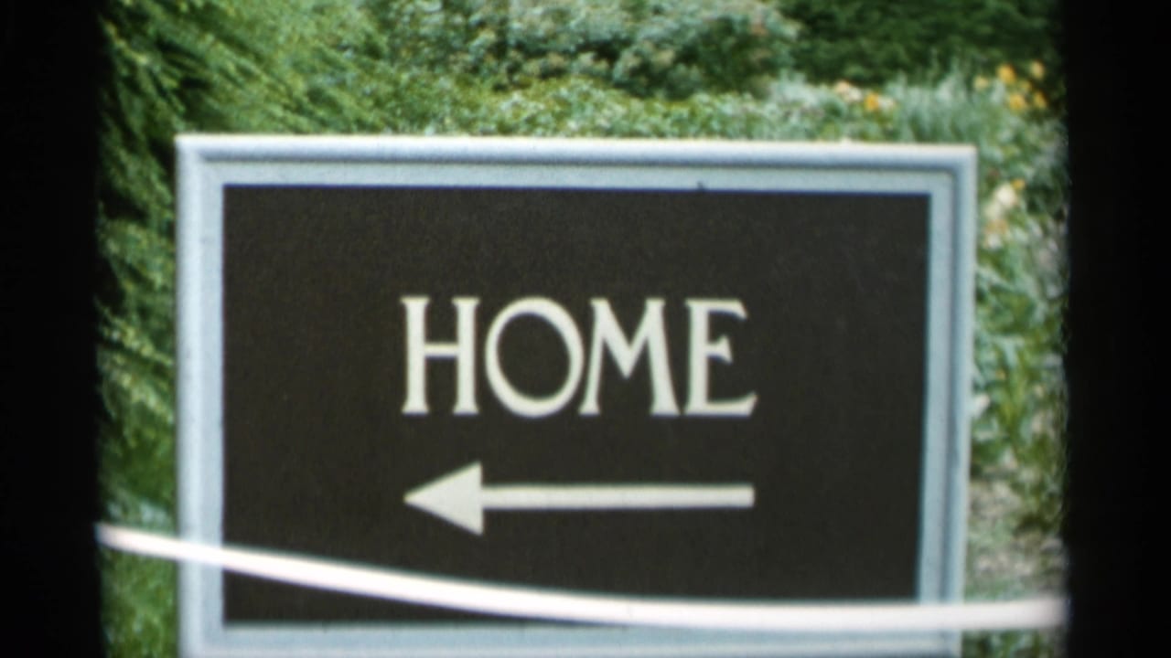 Black sign reading HOME with a left arrow beside green foliage.