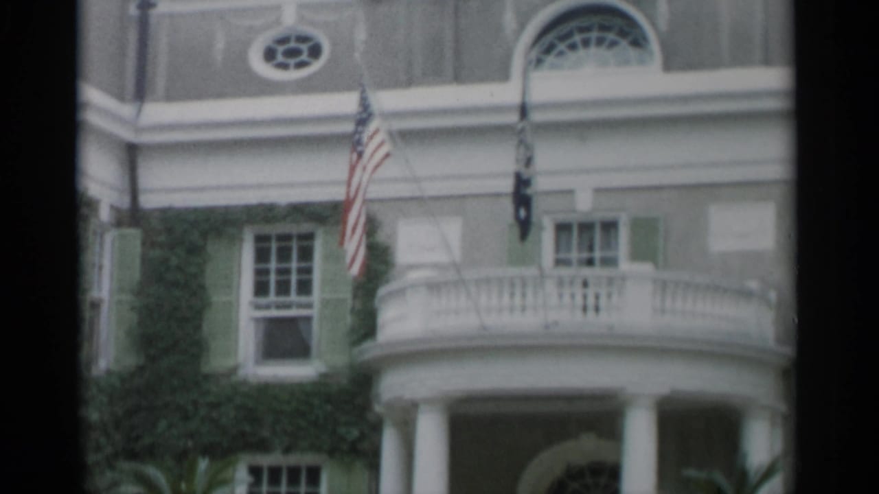 Ivy-covered facade with columns, balcony, green shutters, and American flags.