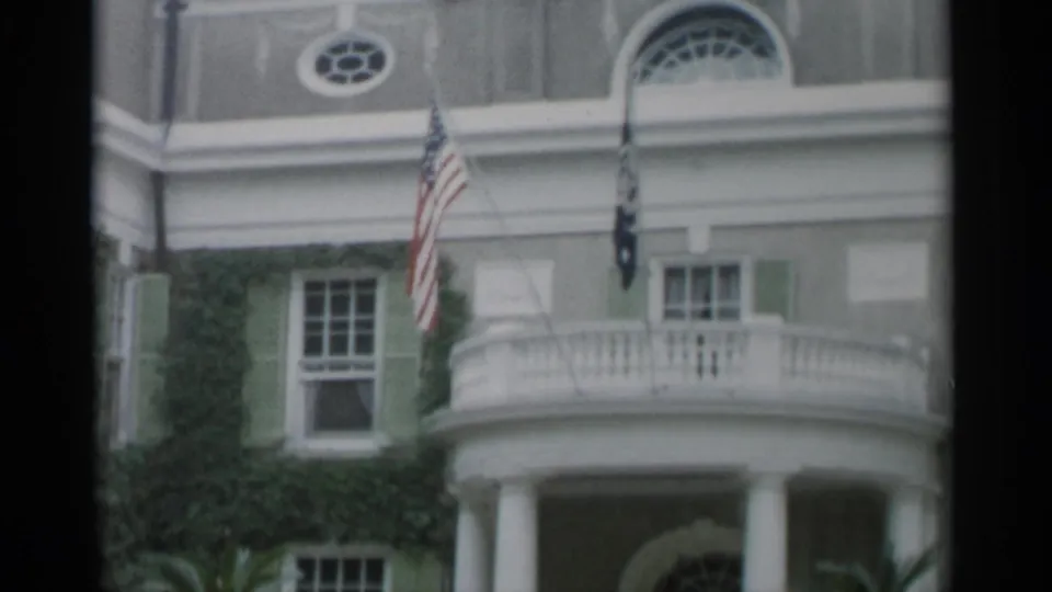 1956 Jones Beach home-movie frame showing an ivy-covered building facade with white columns, a curved balcony, green shutters, and flags.
