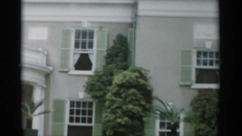 1956 Jones Beach frame showing a side portion of the ivy-covered building with sash windows, green shutters, balcony edge, and planting.