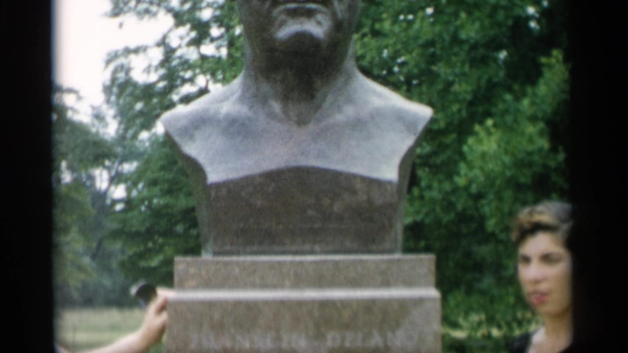 Bronze bust on a stone pedestal with a woman partly visible beside it.