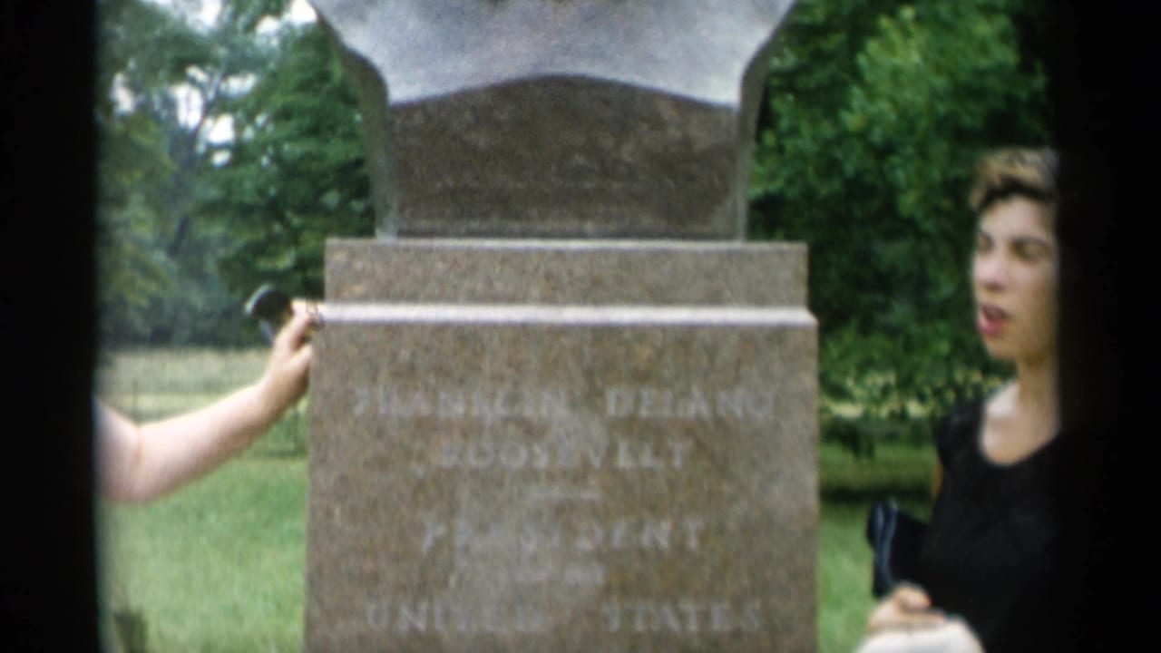 Woman in a dark top stands beside the monument pedestal as a hand touches the inscription.