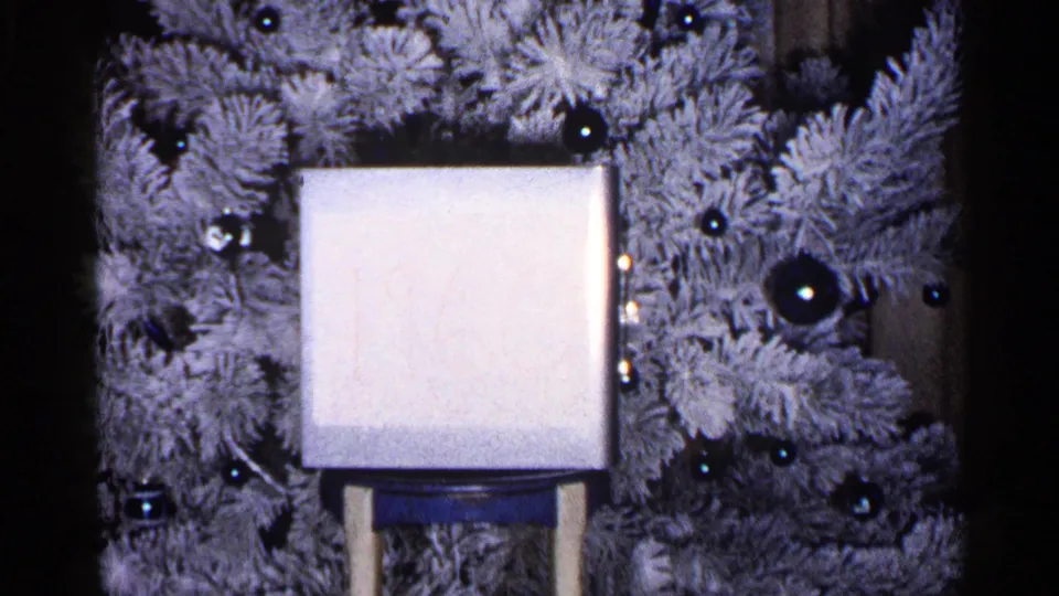 A white gift box sits on a small stand before a flocked Christmas tree in this 1960 Duluth holiday home-movie frame.