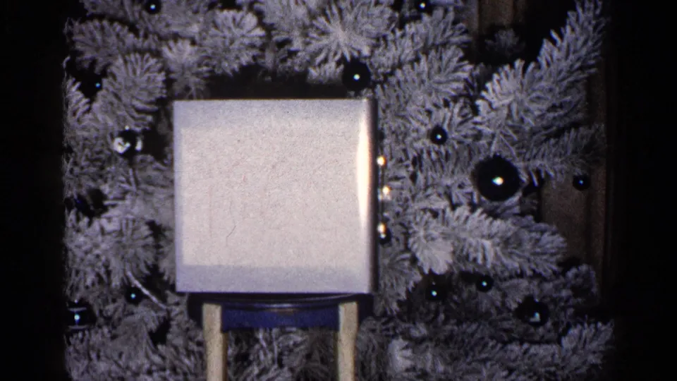 1960 Duluth frame with a stand-mounted square object centered against a flocked Christmas tree and dark ornaments.