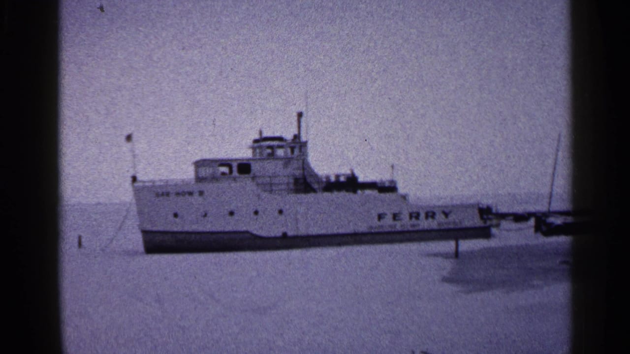 White ferry with FERRY lettering resting on frozen lake ice under a pale sky.