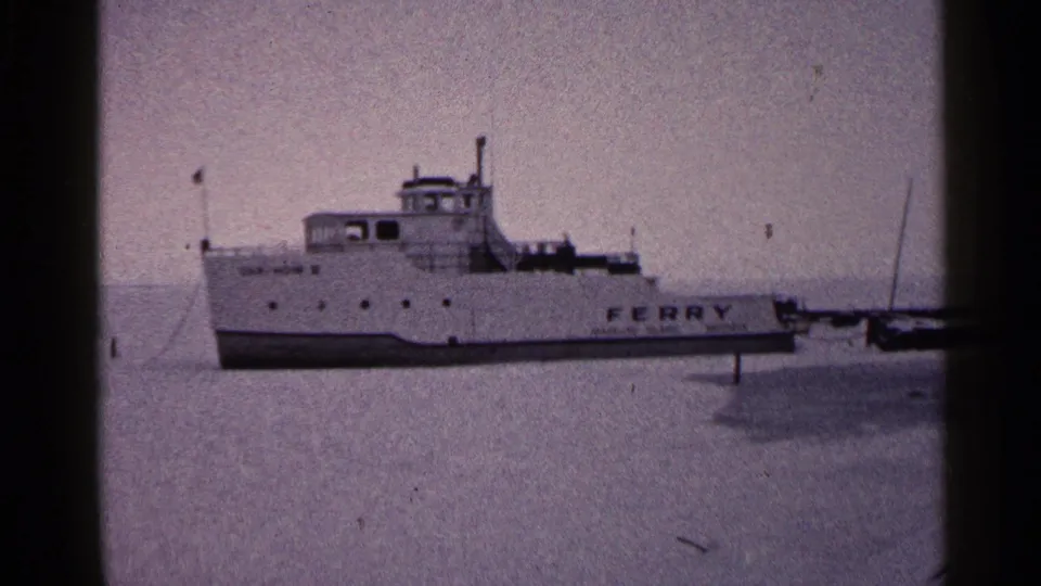 1960 Duluth frame showing the ferry’s side lettering, wheelhouse, hull, frozen lake surface, and adjacent dock structure.