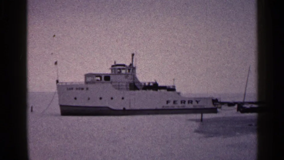 1960 Duluth home-movie still showing the ferry closer in frame on a frozen lake, with soft focus and visible 8mm grain.