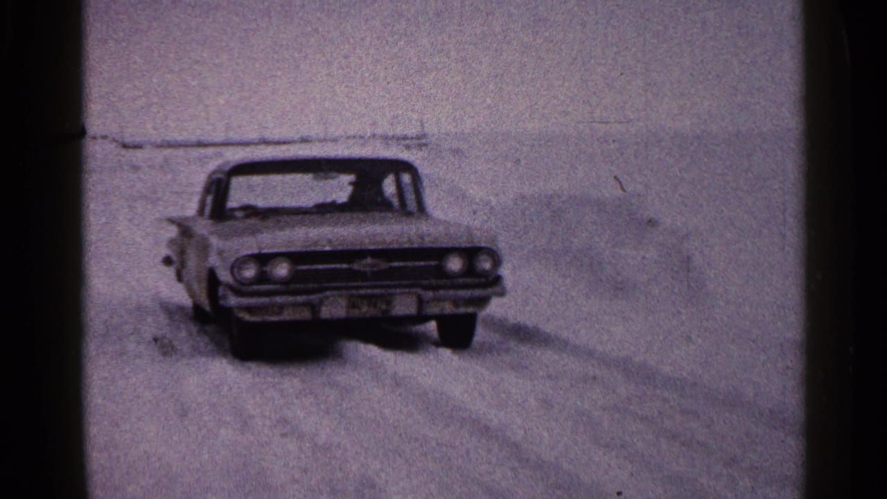 A classic white American sedan approaches across snowy lake ice in a circa-1960 Duluth home movie frame.